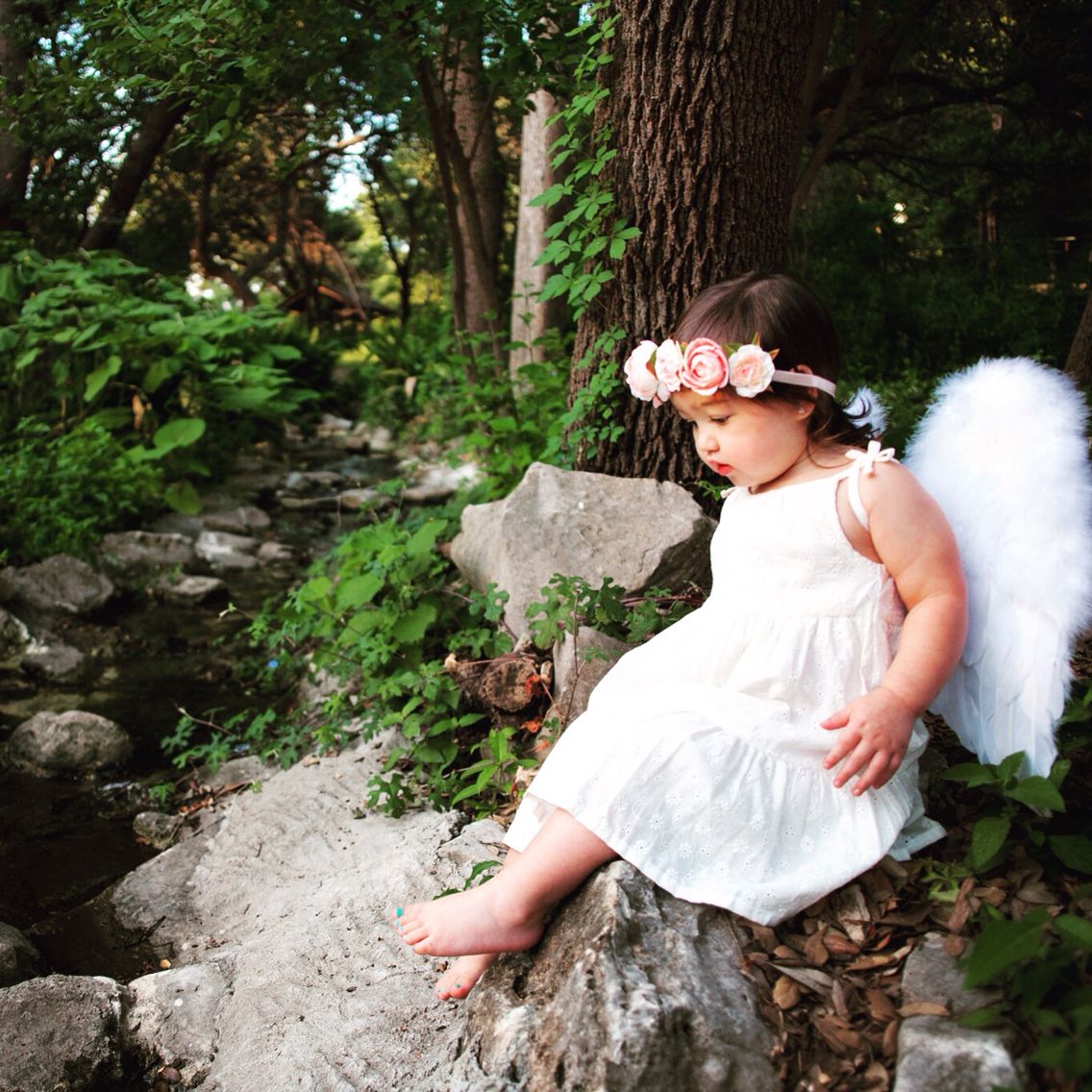 A serene little girl wearing angel wings perches on a rock