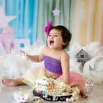 A cute baby girl wearing a tutu and crown, sitting on a cake during a creative photo shoot for her first year