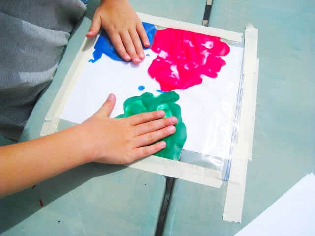 A child's hand delicately touches a paint-smeared paper, showcasing their artistic talent. Easy Finger Painting that is Mess-Free.