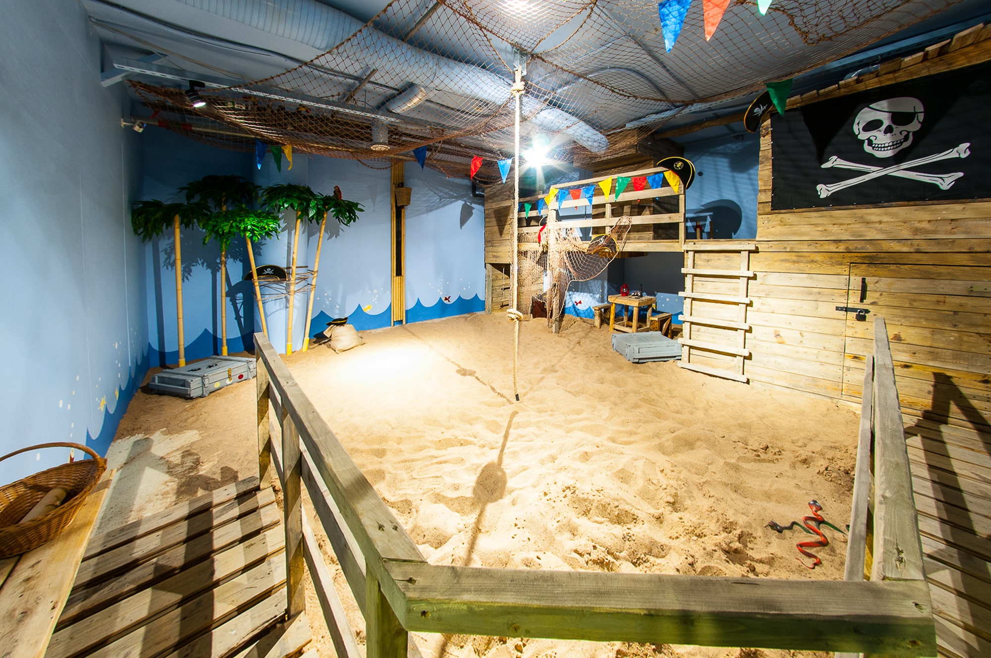 A pirate-themed room with a sand pit and a rope swing, perfect for an adventurous escape room experience for kids
