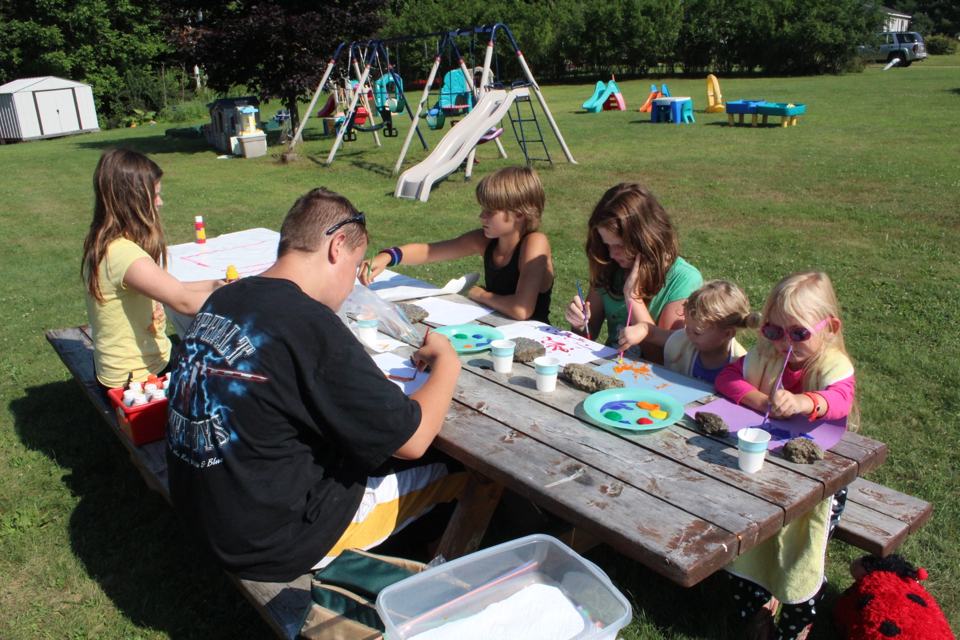 A diverse group of individuals enjoying finger-painting outdoors while sitting at a picnic table