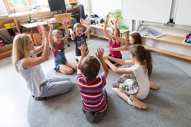 Children sitting in a circle with hands up