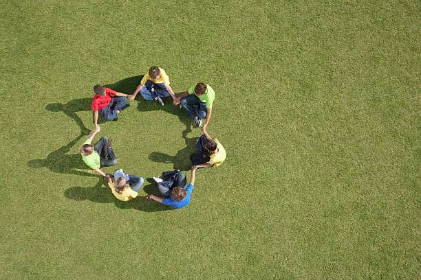 A group of people sitting in a circle on a green field