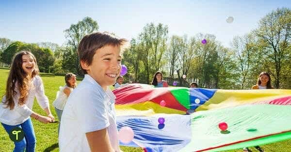 Kids playing with a colorful parachute during a Mini-Olympics Field Day, fostering teamwork and fun.