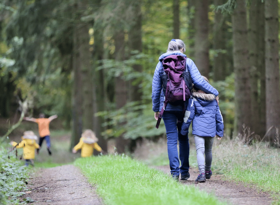 A woman and two children walking through the woods, exploring nature and enjoying a family outing.