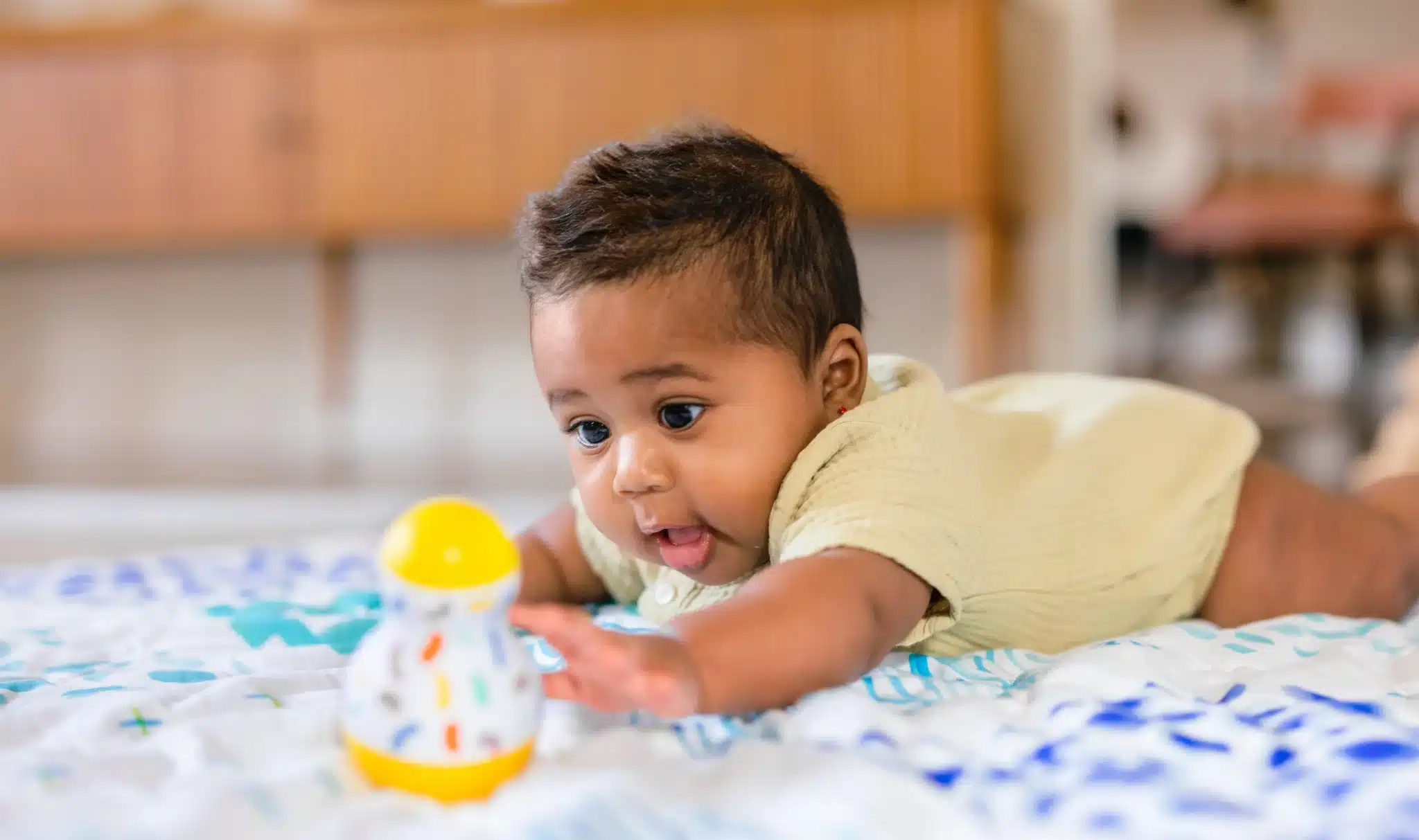 A baby joyfully engages with a toy on a soft blanket, exploring new developments during the 4-6 month stage of growth