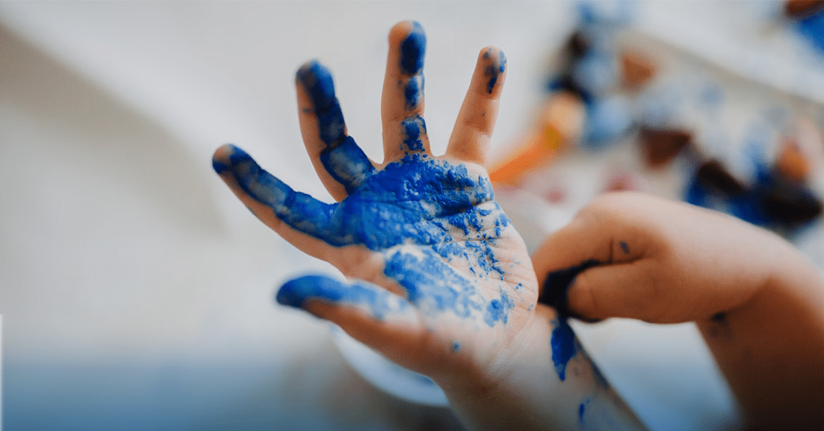 Child's hand covered in blue paint during finger painting activity.