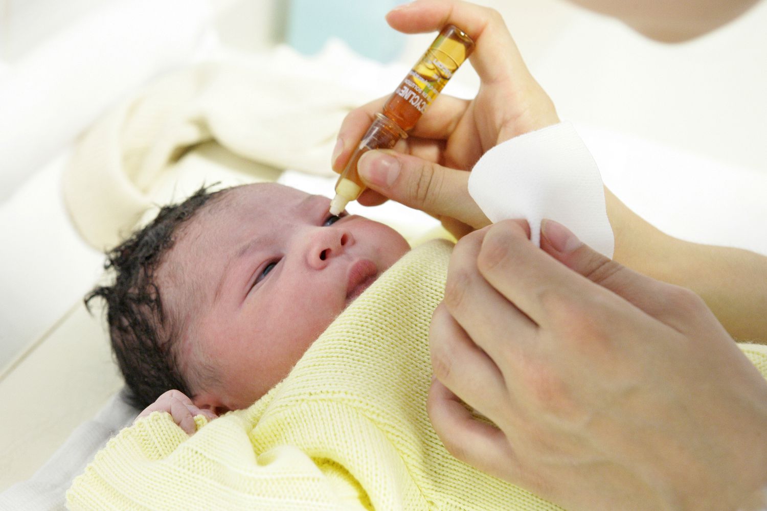 A nurse gently administers an injection to a baby. the pros of giving eye medicine to newborns.