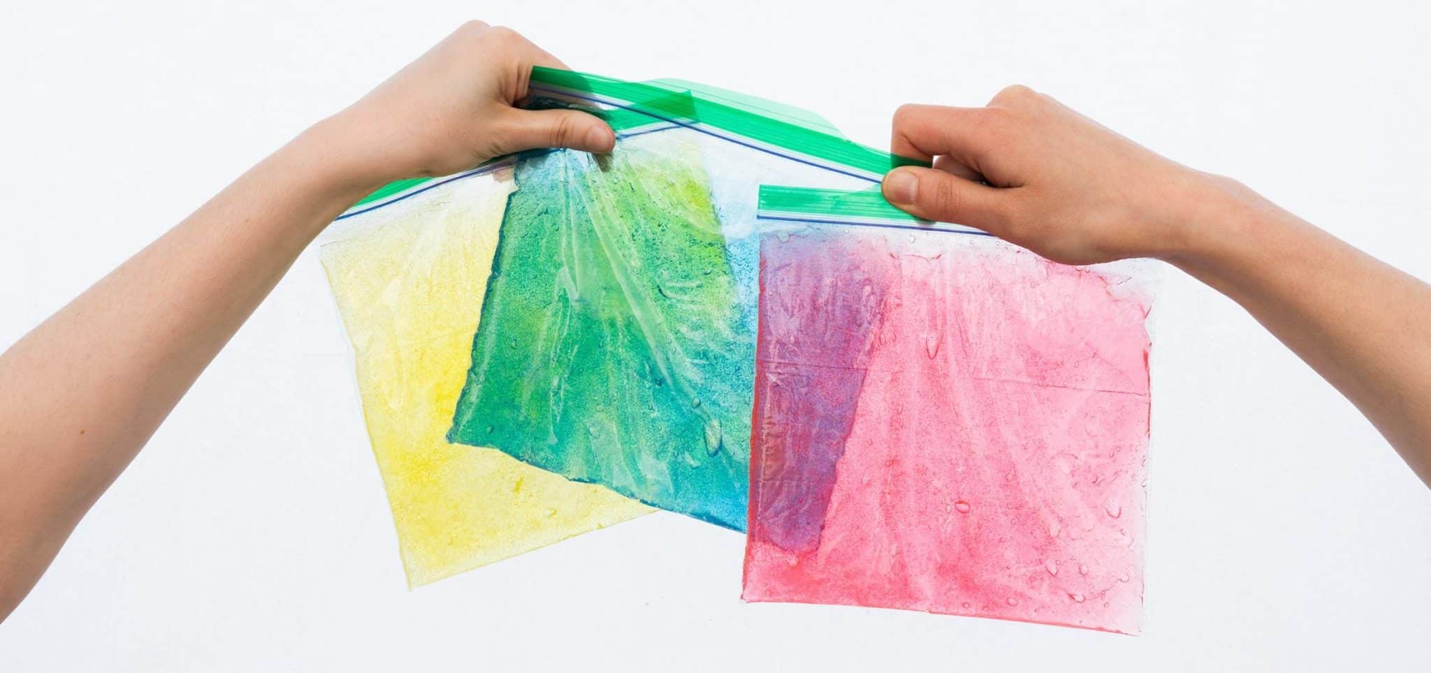 Two hands holding colored paper bags, sealed in a Ziploc bag.