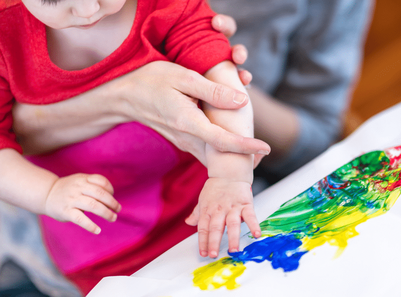 A child holding a woman's hand while painting with washable paint.