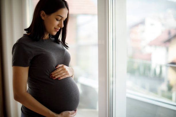 A pregnant woman stands by the window