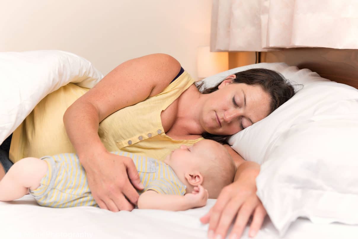 A woman and baby peacefully resting together in bed, illustrating the topic of improving baby's sleep