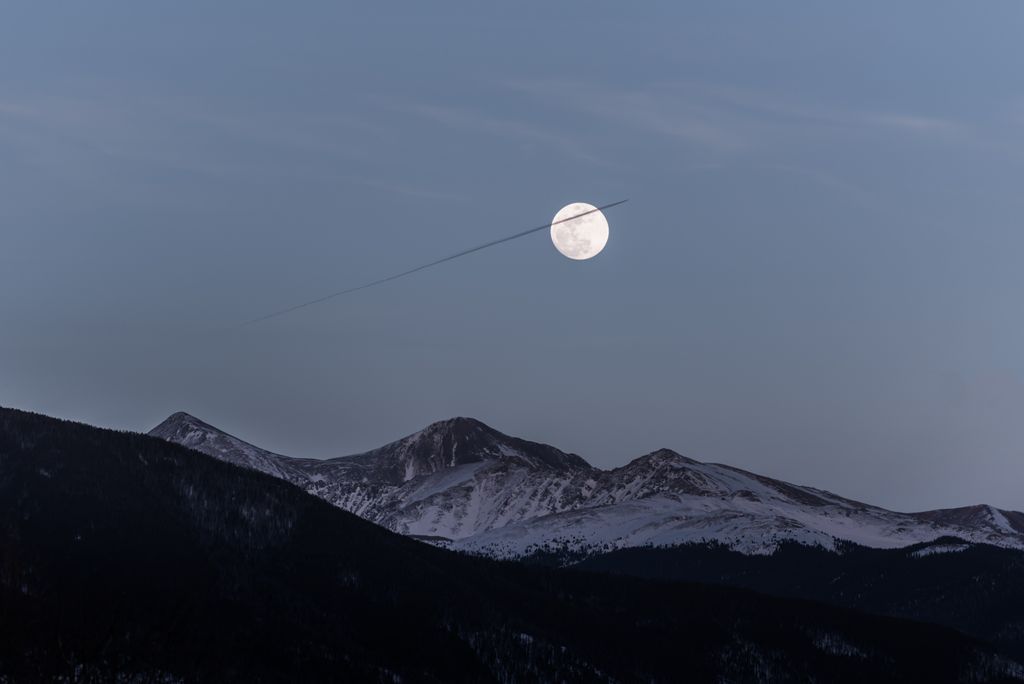 A plane soaring above moonlit mountains, creating a captivating nocturnal scene