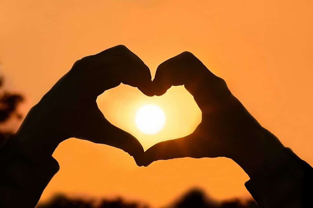 Hands forming heart shape with sun in background - symbolizing love and warmth in the digital age