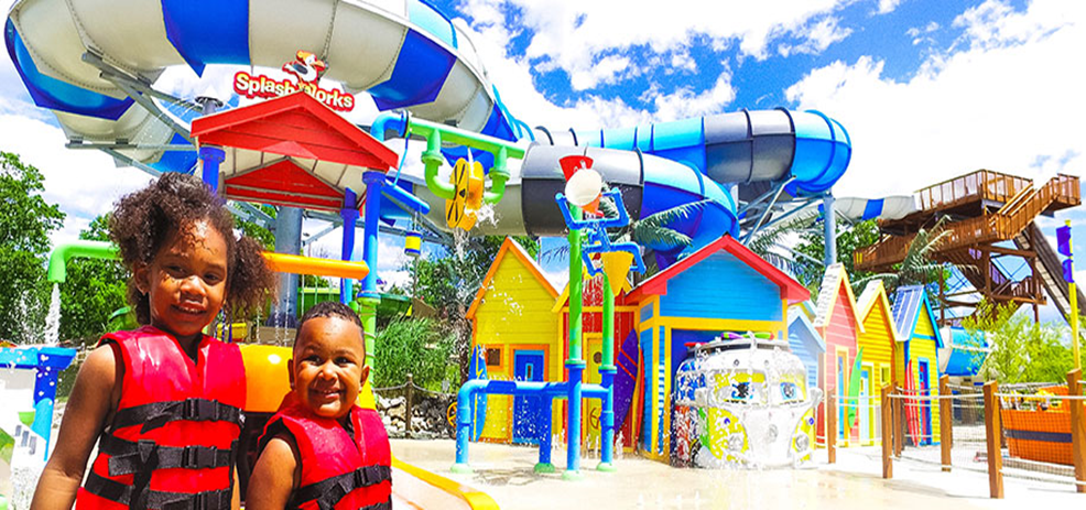 Two children in life jackets excitedly stand in front of a water park, ready to enjoy its top attractions