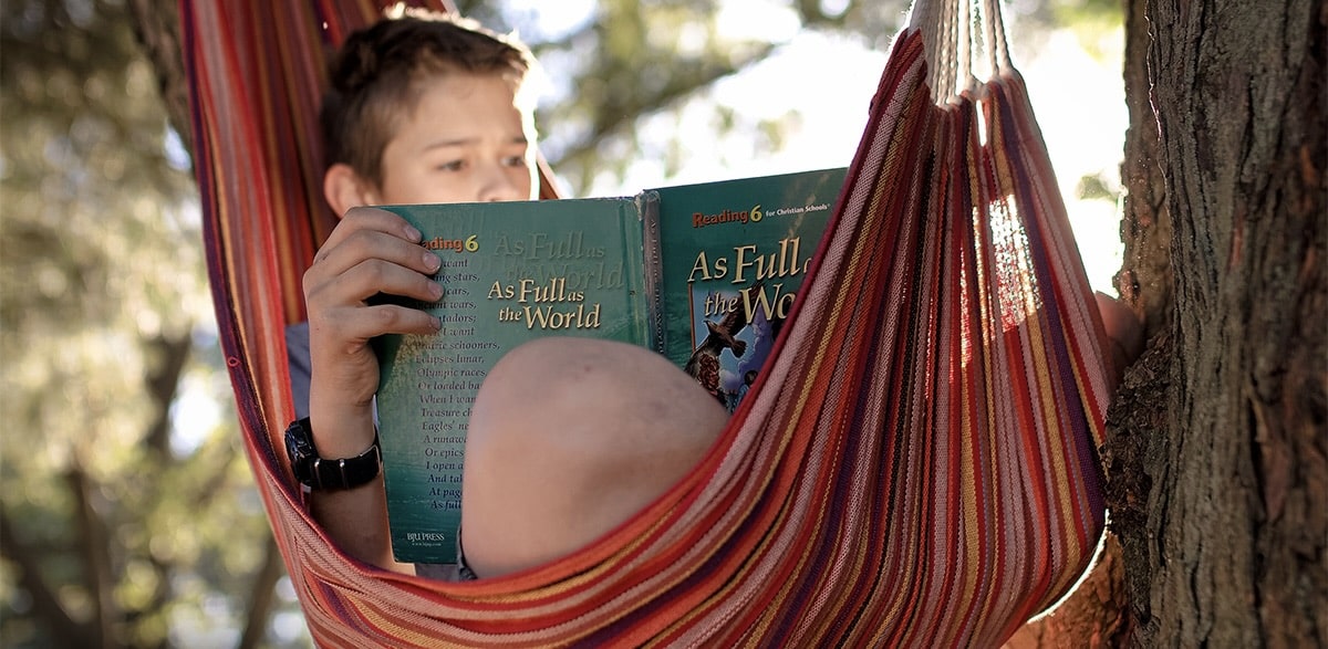 a boy sitting on a hammock swing and reading book