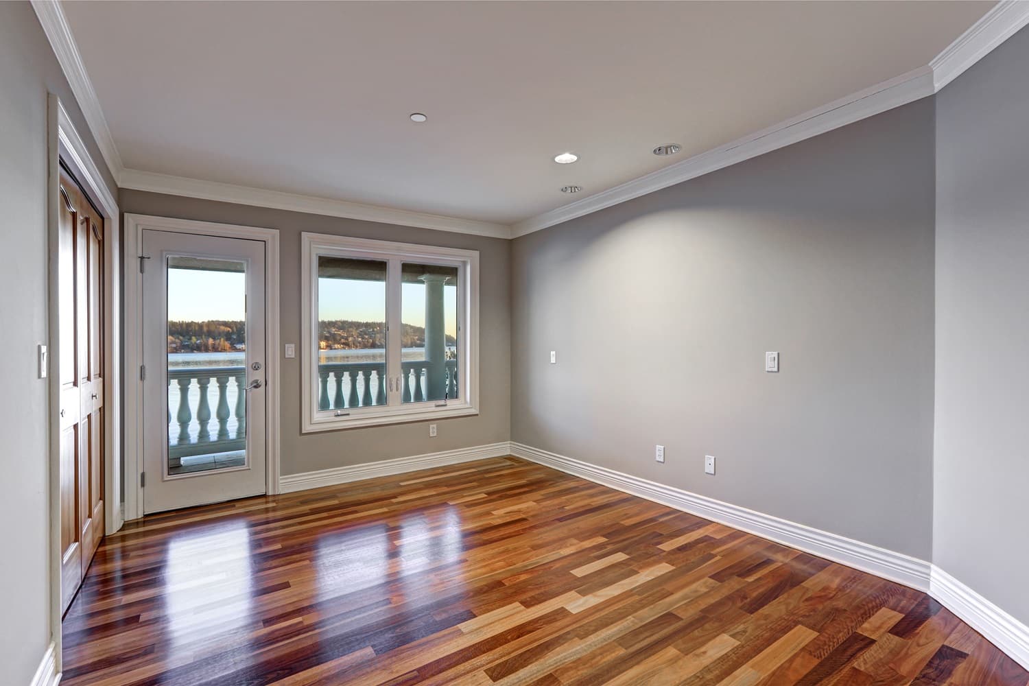 Empty room interior with soft grey walls paint color, glossy hardwood floor and door to balcony. Northwest, USA